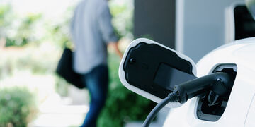 Are EV cars affecting your car resale value? Car being charged in foreground with man walking in background