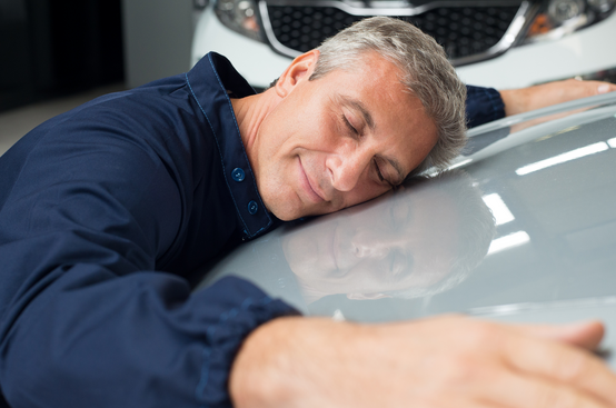 Man fulfilling his dream of buying a new car and giving it a big hug