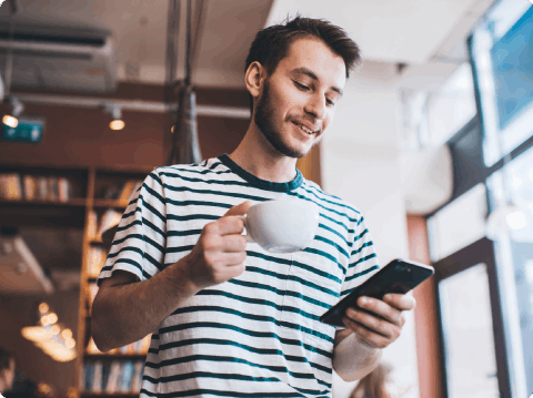 A man holding a cup of coffee and looking down at his mobile phone