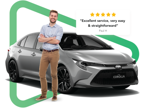 Brown haired white man in blue shirt smiling and standing with crossed arms in front of a grey Toyota sedan.
